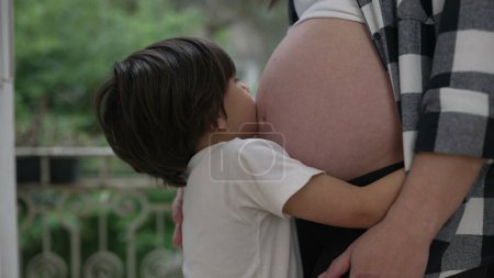 Lindo niño pequeño abrazando el vientre embarazada de la madre mostrando amor y afecto durante la última etapa del embarazo