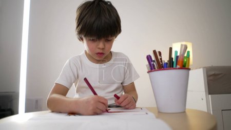 Child drawing on paper with coloring pen. 5-year-old boy engrossed in creative art work, concentrated kid