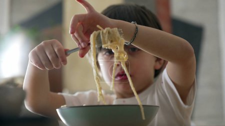 Spaghetti delight - Little boy attempting to spin fork while eating pasta food during mealtime. Child enjoying learn to use utensils