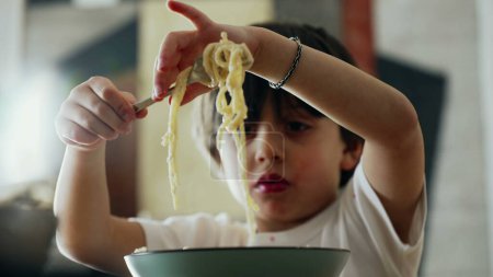 Foto de Delicia de espaguetis - Pequeño niño aprendiendo a girar tenedor mientras come pasta, disfrutando del uso de utensilios para la hora de comer - Imagen libre de derechos