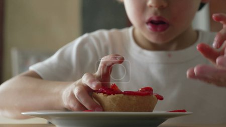 Téléchargez les photos : Un petit garçon dégustant un dessert au fromage. 5 ans enfant saisissant la nourriture sucrée de l'assiette - en image libre de droit