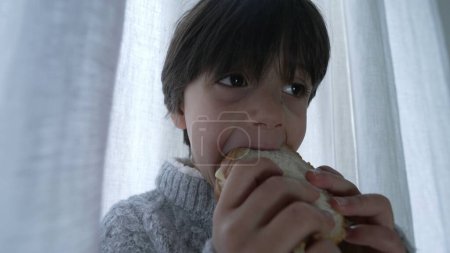 Child snacking sandwich, close-up hand and face of one small boy eating rich carb food in the afternoon