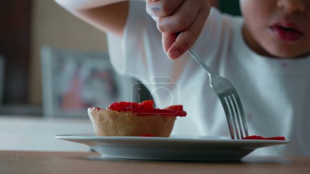 Téléchargez les photos : Lutte de l'enfant pour atteindre Cheesecake à la fourchette - Gros plan sur les friandises sucrées garnies de fraises sur une assiette - en image libre de droit