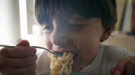 Pâtes alimentaires pour enfants, petit garçon de 5 ans affamé mange de la nourriture carb, enfant dégustant des spaghettis au fromage, gros plan sur le visage et de la nourriture