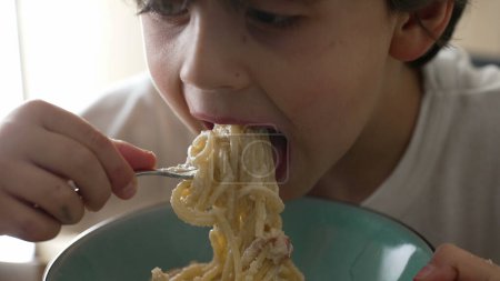 Pâtes alimentaires pour enfants, petit garçon de 5 ans affamé mange de la nourriture carb, enfant dégustant des spaghettis au fromage, gros plan sur le visage et de la nourriture
