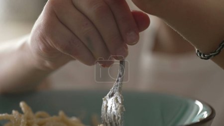 Child spinning spaghetti with fork close-up hand and face. Little boy learning to eat pasta, carb-rich food