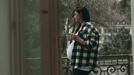 Photo for Reflective Pregnant Woman at Apartment Balcony, holding warm drink, looking at Scenic View in Solitude, Cherishing Tranquil Moments in Third Trimester - Royalty Free Image