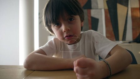 Photo for Assertive child hits table surface with hand. 5 year old boy demanding attention while looking at camera, close-up face and fist - Royalty Free Image