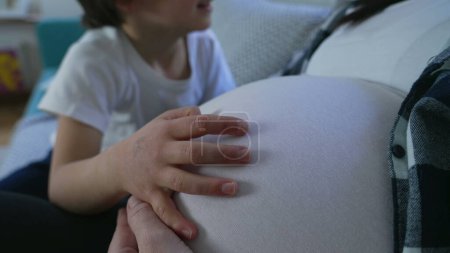 Child's hand resting on top of mother's pregnant belly during third trimester of pregnancy, maternal concept between brother and unborn baby, gentle touch