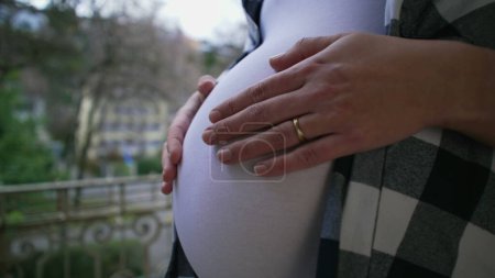 Téléchargez les photos : Amour maternel - femme enceinte qui attend des caresses pour nouveau-né 8 mois ventre par appartement balcon, main close-up caresse tendre - en image libre de droit