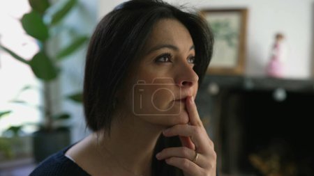 Pensive Woman in Her 30s Contemplating, Close-Up of Face in Deep Thought, Indoor Home Setting. Person seeking solution to problem in thoughtful manner
