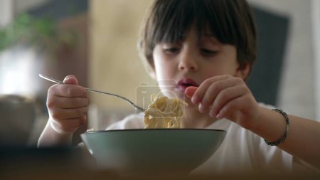 Spaghetti delight - Little boy attempting to spin fork while eating pasta food during mealtime. Child enjoying learn to use utensils