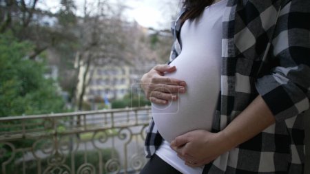 Schwangere Mutter streichelt 8 Monate alten Bauch vom Balkon der Wohnung und zeigt Liebe und Zuneigung, wenn sie ein Neugeborenes erwartet