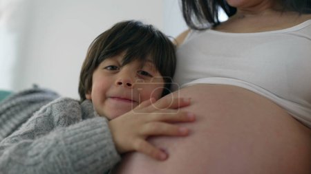 Foto de Momento tierno con un niño de 5 años besando amorosamente el vientre de la madre, posando para una foto de cerca, celebrando el vínculo familiar en el embarazo en la etapa tardía - Imagen libre de derechos