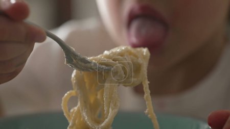 Child spinning spaghetti with fork close-up hand and face. Little boy learning to eat pasta, carb-rich food