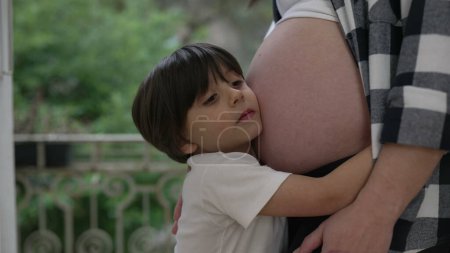 Cute little boy hugging mother's pregnant belly showcasing love and affection during late stage of pregnancy