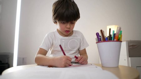 Child drawing on paper with coloring pen. 5-year-old boy engrossed in creative art work, concentrated kid
