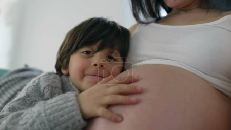 Photo for Tender Moment with 5-Year-Old Boy Lovingly Kissing Mother's Belly, Posing for a Close-Up Photo, Celebrating Family Bond in Late Stage Pregnancy - Royalty Free Image