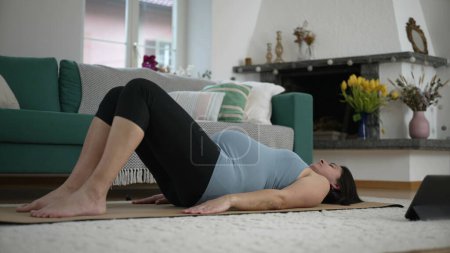 Téléchargez les photos : Femme enceinte faisant de l'exercice de yoga à la maison salon, prendre soin des maux de dos pendant la routine d'entraînement prénatal - en image libre de droit