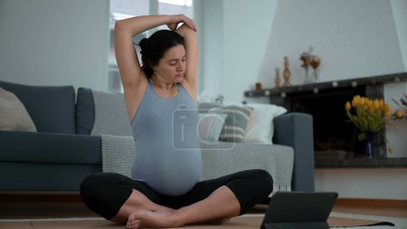 Photo for Expectant 30s Mother Engaging in Living Room Wellness Exercises - Late Stage Pregnancy Routine with Digital Tablet Guidance, Prioritizing Body Comfort and Health - Royalty Free Image