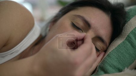 Foto de Mujer de 30 años agotada acostada en la cama tratando de descansar sintiendo fatiga frotando la cara con los ojos cerrados. Siesta de persona - Imagen libre de derechos