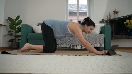 Yoga en el Hogar para Madres Embarazadas - Mujer de 30 Algo Enfocándose en Posadas Prenatales en la Sala de Estar, Cultivando Bienestar y Serenidad en el Embarazo Tardío delante de la guía del dispositivo de tableta