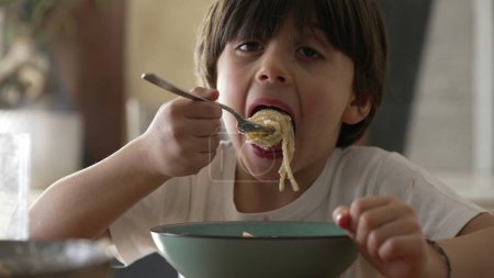 Small boy eating spaghetti during mealtime. Close-up face of child enjoying carb rich food pasta