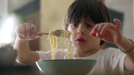 Téléchargez les photos : Joie au repas - Gros plan sur un petit garçon dégustant des spaghettis et savourant des pâtes riches en glucides - en image libre de droit