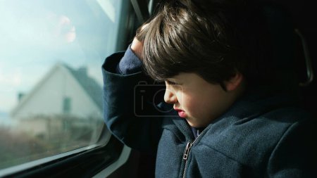 Photo for One small boy seated by train window looking at landscape scenery pass by while squinting his eyes protecting against sunrays. 5 year old caucasian kid traveller - Royalty Free Image