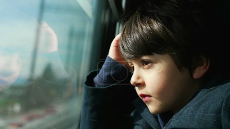Pensive Kind, das mit dem Zug unterwegs ist und die vorbeiziehende Landschaft betrachtet, Profil Nahaufnahme eines 5-jährigen Jungen, der beim Tagträumen auf den Blick aus dem Inneren eines Hochgeschwindigkeitszuges starrt
