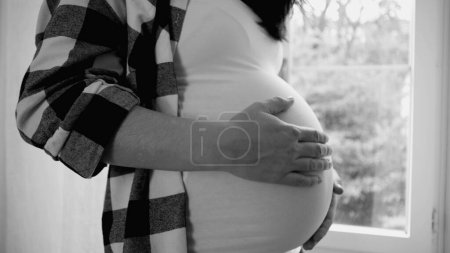 Foto de Escena de embarazo dichosa, mujer alegre embarazada tocando suavemente su vientre embarazada de 8 meses, soñando con el recién nacido en blanco y negro, monocromo - Imagen libre de derechos
