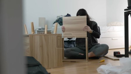 Expertise in der Möbelmontage erfasst - Spirited Woman baut Nachttisch, Betonung der DIY-Techniken im Wohndekor, die die Aufregung des Umzugs und der Personalisierung eines neuen Raumes widerspiegeln