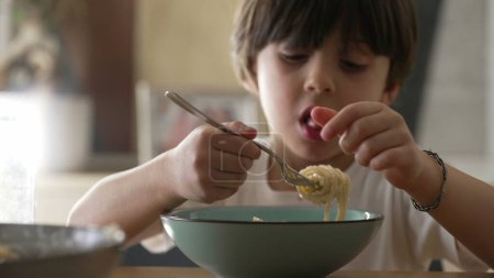 Téléchargez les photos : Petit garçon mangeant des spaghettis pendant les repas. Gros plan sur le visage de l'enfant dégustant des pâtes riches en glucides - en image libre de droit