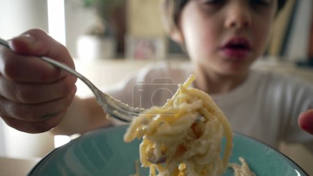 Gros plan du petit garçon filant des pâtes spaghetti à la fourchette. Enfant de 5 ans mangeant de la nourriture riche en glucides pendant les repas, enfant apprenant à manger un plat italien
