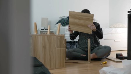 Furniture Assembly Expertise Captured - Spirited Woman Building Nightstand, Emphasizing DIY Techniques in Home Decor, Reflecting the Excitement of Relocating and Personalizing a New Space