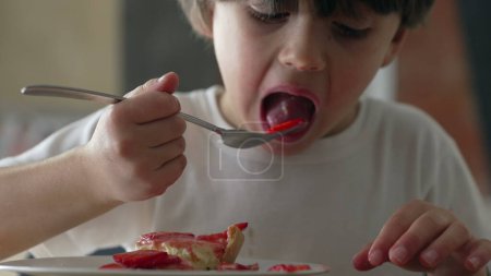 Niño comiendo trozos de fresa con tenedor, niño disfruta de postre dulce después de la hora de la comida, niño meticulosamente la selección de rebanadas de fruta de pastel de queso