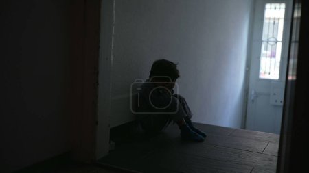 Photo for One depressed little boy seated in dimly lit corridor covering face with hands feeling despair and sadness during family crisis - Royalty Free Image