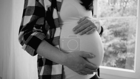 Foto de Escena de embarazo dichosa, mujer alegre embarazada tocando suavemente su vientre embarazada de 8 meses, soñando con el recién nacido en blanco y negro, monocromo - Imagen libre de derechos