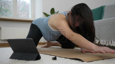 Photo for Pregnant woman stretching body in while on Yoga man at living room floor. expectant mother taking care of back relief in front of table device - Royalty Free Image