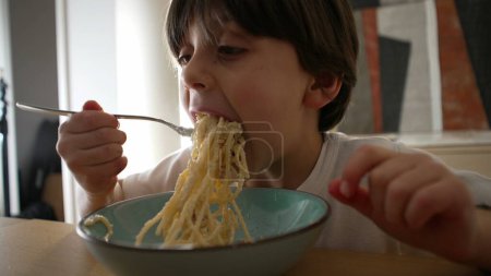 Kind isst Spaghetti, unordentlicher kleiner Junge spinnt nachts Nudeln mit Gabel