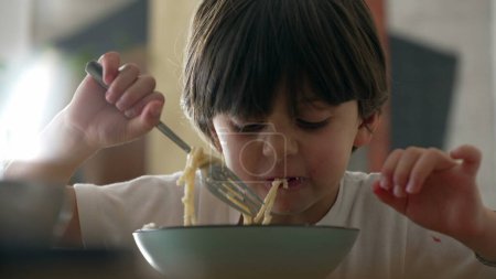 Téléchargez les photos : Joie au repas - Gros plan sur un petit garçon dégustant des spaghettis et savourant des pâtes riches en glucides - en image libre de droit