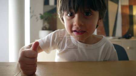 Niño pequeño golpeando la mesa con el puño mientras mira la cámara. Niño exigiendo concepto de atención