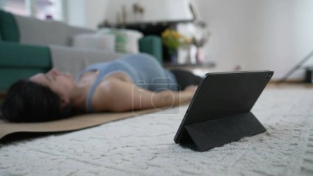 Foto de Mujer embarazada estirando el cuerpo mientras está en la esterilla de yoga en el piso de la sala de estar. madre embarazada cuidando el alivio de la espalda delante del dispositivo de mesa - Imagen libre de derechos