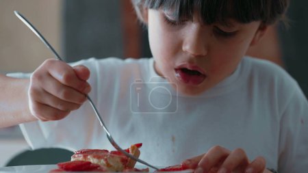 Téléchargez les photos : Jeune Garçon Sélection délicate de tranches de fraise de Cheesecake / Savourer un dessert sucré à la fourchette après le dîner - en image libre de droit