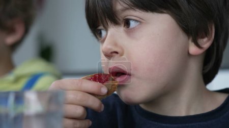 Close-up face of small boy eating bread with jelly for breakfast, candid kid snacking carb food