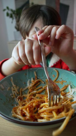 Foto de Niño girando espaguetis con tenedor, primer plano de la mano. Niño comiendo pasta para la cena, comida italiana. Vídeo vertical - Imagen libre de derechos