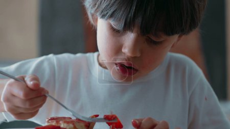 Junge wählt Erdbeerscheiben aus Käsekuchen / Süßes Dessert mit Gabel nach dem Abendessen