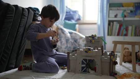 Téléchargez les photos : Petit garçon jouant dans la chambre avec château jouet à la maison portant un pyjama. Enfant absorbé dans le jeu imaginatif dans le jeu du matin - en image libre de droit