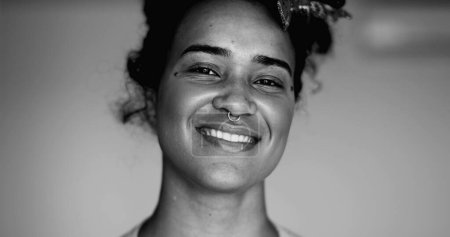 Monochromatisches Porträt einer glücklichen jungen schwarzen Brasilianerin, die mit freundlicher Demeanor lächelt, fröhliche Großaufnahme auf weißem Hintergrund, schwarz-weiß