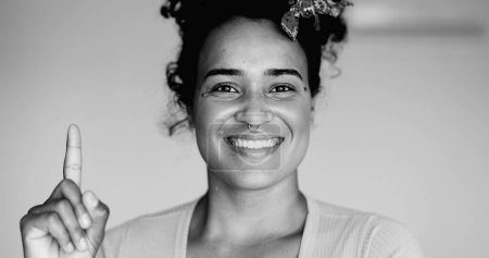 Foto de Joven mujer afroamericana monocroma primer plano de alegre latina negra con idea, dedo apuntando hacia arriba en blanco y negro - Imagen libre de derechos